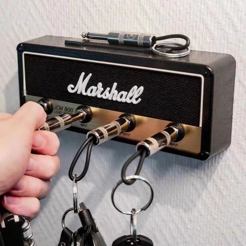 A wall-mounted vintage Fender guitar amp key holder, crafted from durable zinc alloy and equipped with a 6.35mm audio plug. Comes with four keyrings with P10 plugs, a wall mounting kit, and user-friendly instruction manual. Perfect gift or décor for music enthusiasts and a creative solution for key storage in home, office, studio, and rehearsal settings. Weighs 72 grams and measures 21.5cm in length. Colors may vary slightly due to screen differences.
