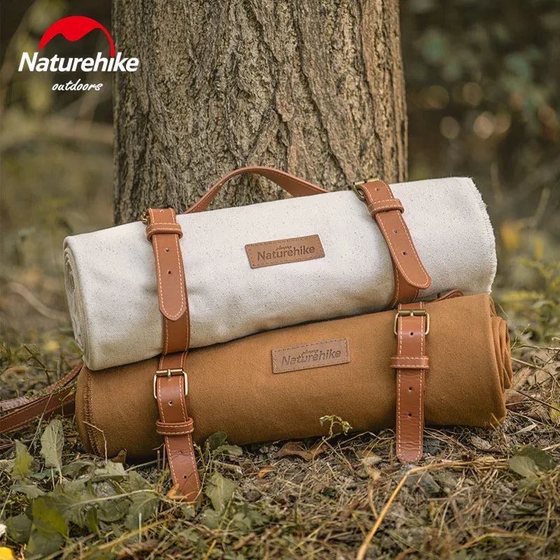 An image showing the ultra-light outdoor camping and picnic waterproof canvas blanket, elegantly blending in shades of white and brown. This lightweight, durable blanket can be seen rolled and packed in a robust PE bag, finished with stylish leather strapping. Perfect for all types of outdoor activities like camping, picnics or travels, its 100% cotton fabric ensures both comfort and longevity.