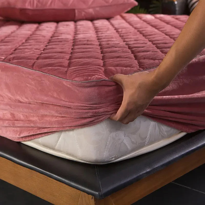 A luxurious, quilted velvet mattress cover in warm crystal tones spread over a queen or king-sized bed. The plush texture of the mattress cover indicates its softness and coziness, providing superior comfort for sleeping. Ideal for thicker mattresses, its thick coverage giving an impression of a perfect bedsheet replacement for colder nights or for people who prefer a warmer slumber environment. Note, the image does not include a matching pillowcase which is available for separate purchase.