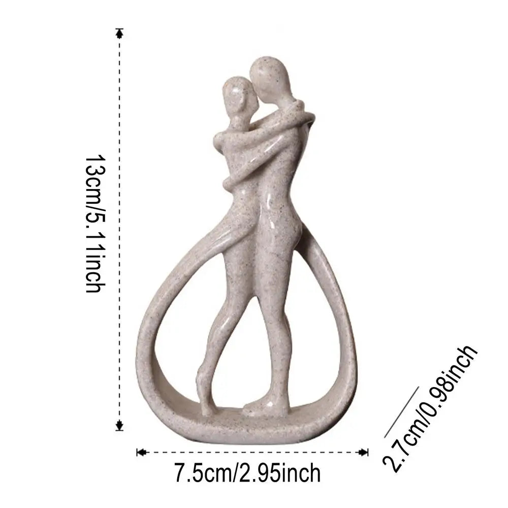 A modern abstract hugging couple statue made from a smooth material showcasing simple lines and a minimalist design, placed delicately on a table in a tastefully decorated living room. The sculpture adds an artistic flair to the room, enhancing the aesthetic appeal while also symbolizing love and connection. It pairs well with other modern or contemporary home decor and can also serve as a stylish ornament in a bedroom or office space.